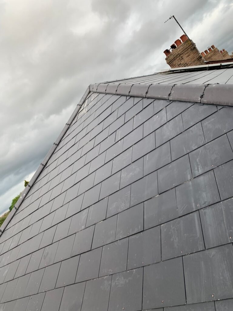 Slate roof slope with chimney stack under a cloudy sky in Hounslow